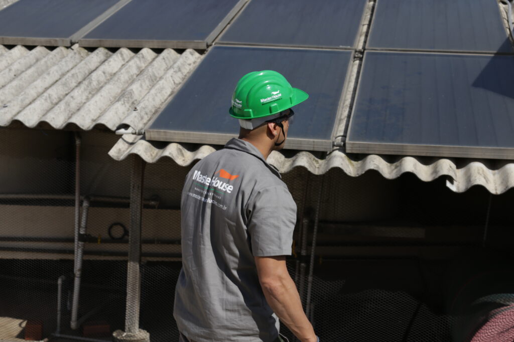 Profissional da Master House em uniforme observando painéis solares, destacando a econômia em energia sustentável.
